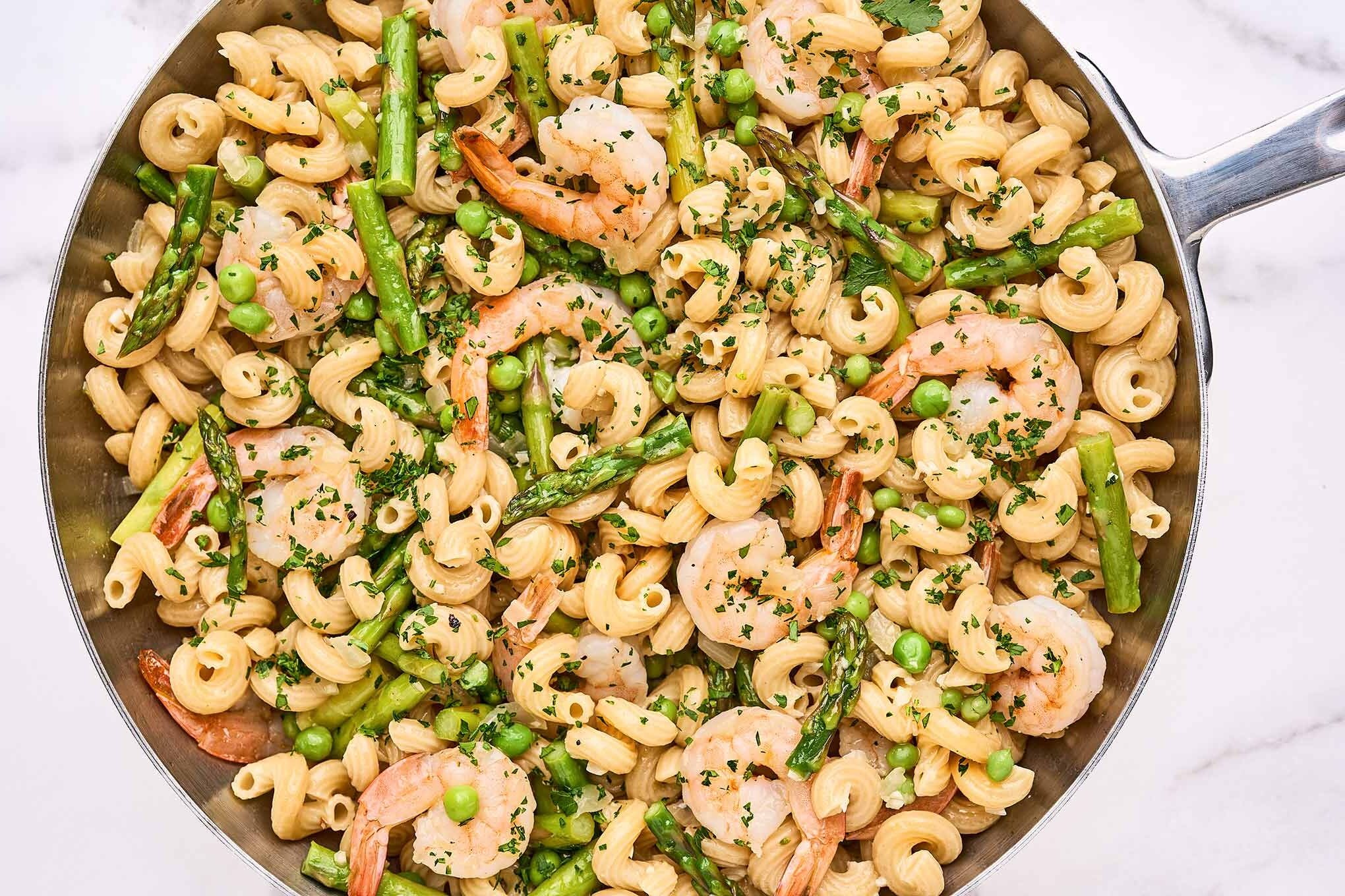 A stainless saut&eacute; pan filled with corkscrew pasta combined with saut&eacute;ed shrimp, asparagus, peas, and parsley, in a light white wine sauce.