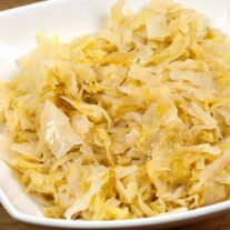 A serving bowl of butter braised cabbage, stockpot in the background, wooden spoon in front.