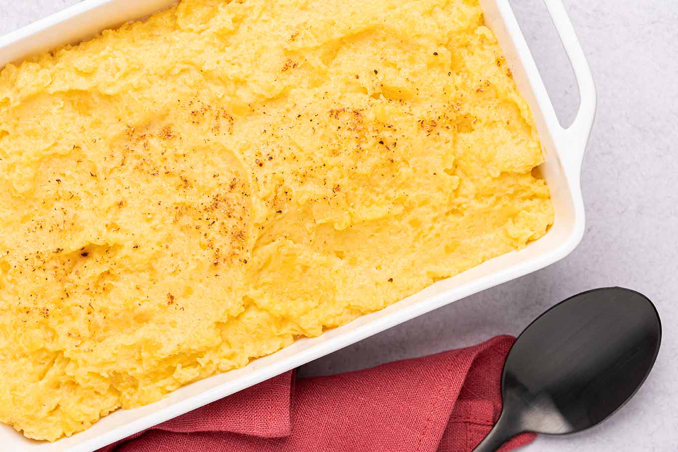 A casserole dish of creamy mashed rutabagas garnished with a sprinkling of nutmeg.