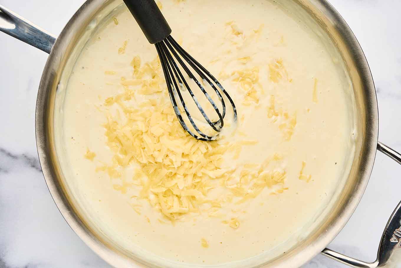 Grated French cheeses being added to b&eacute;chamel sauce for French macaroni and cheese.