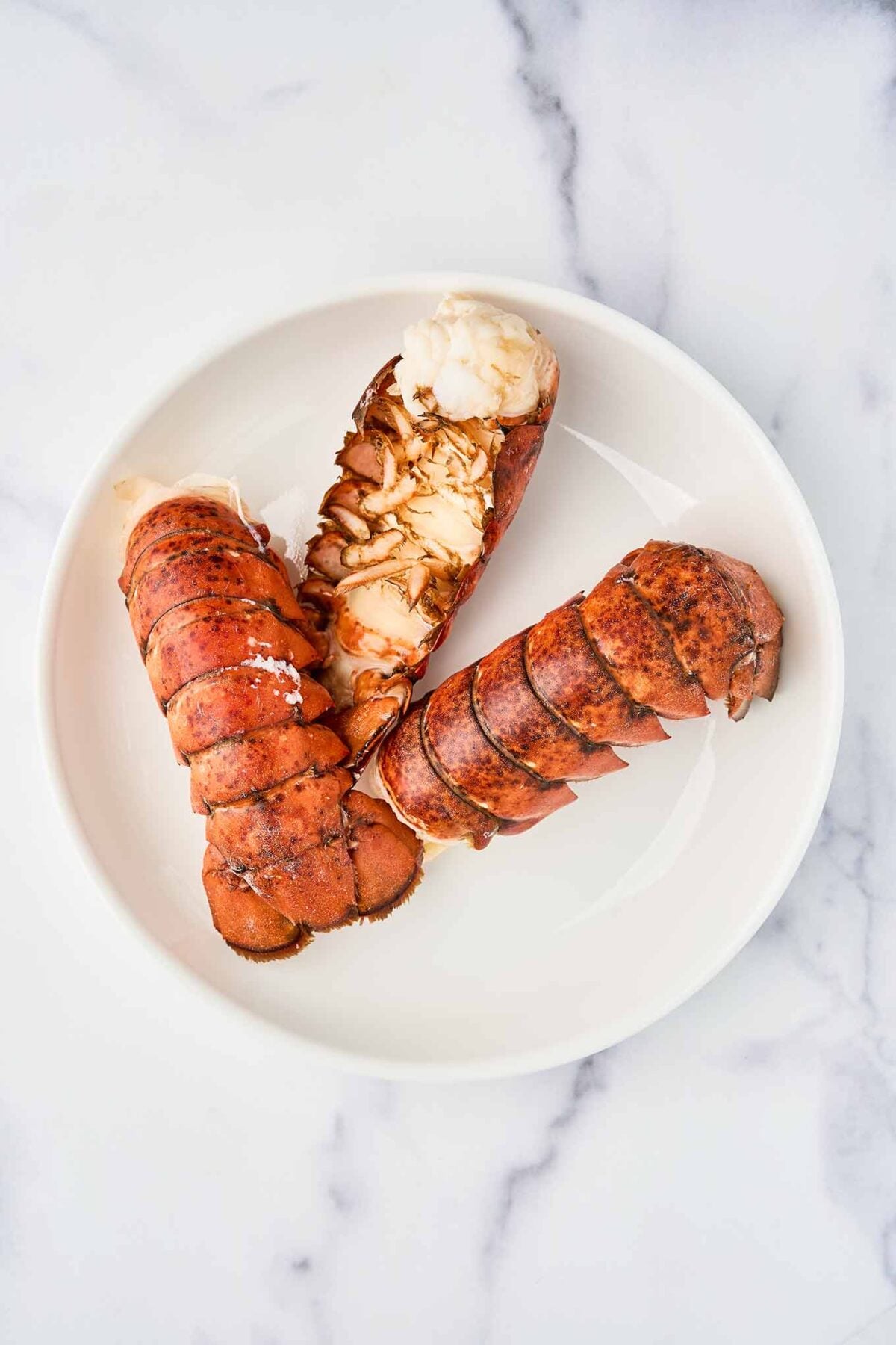 Simmered lobster tails for stovetop lobster mac and cheese, with one shell opened to show the cooked lobster meat.
