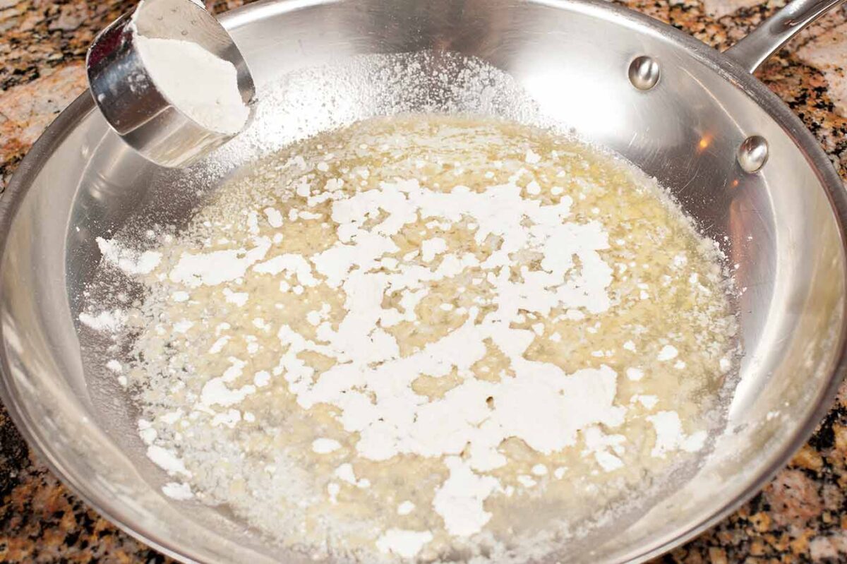 Flour being added to melted butter to make a roux for homemade macaroni and cheese.