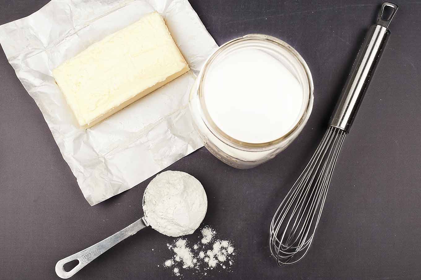 Ingredients for béchamel sauce including butter, flour, whole milk, and a whisk for homemade macaroni and cheese.