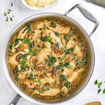 A skillet of chicken, mushrooms, and spinach in a light pan sauce with cheese, mashed potatoes for serving on the side.