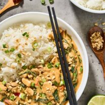 Thai peanut curry with chicken, spinach, jasmine rice, scallions, and chopped peanuts in a white bowl.