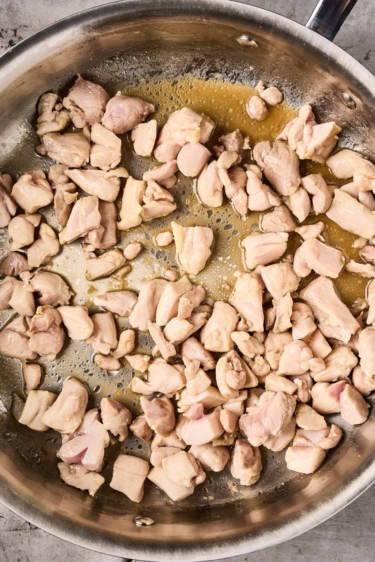 Chicken thighs sautéing in a skillet for Thai peanut curry.