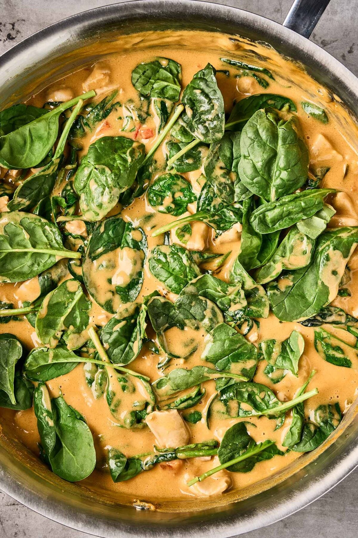 Fresh spinach wilting into creamy Thai peanut curry with chicken in a sauté pan.