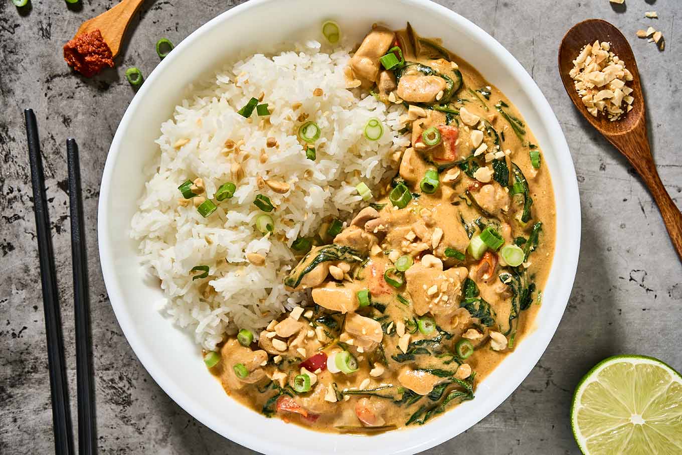 Thai peanut curry with chicken, spinach, jasmine rice, scallions, and peanuts served in a shallow bowl.