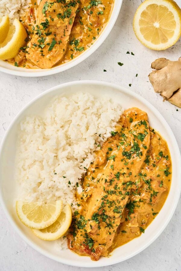 Coconut curry salmon and basmati rice served with creamy curry sauce, fresh cilantro, and lemon wedges.