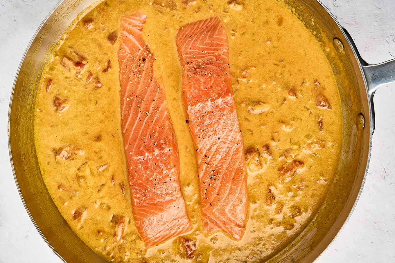Seasoned salmon fillets nestled into the homemade coconut curry sauce before cooking.