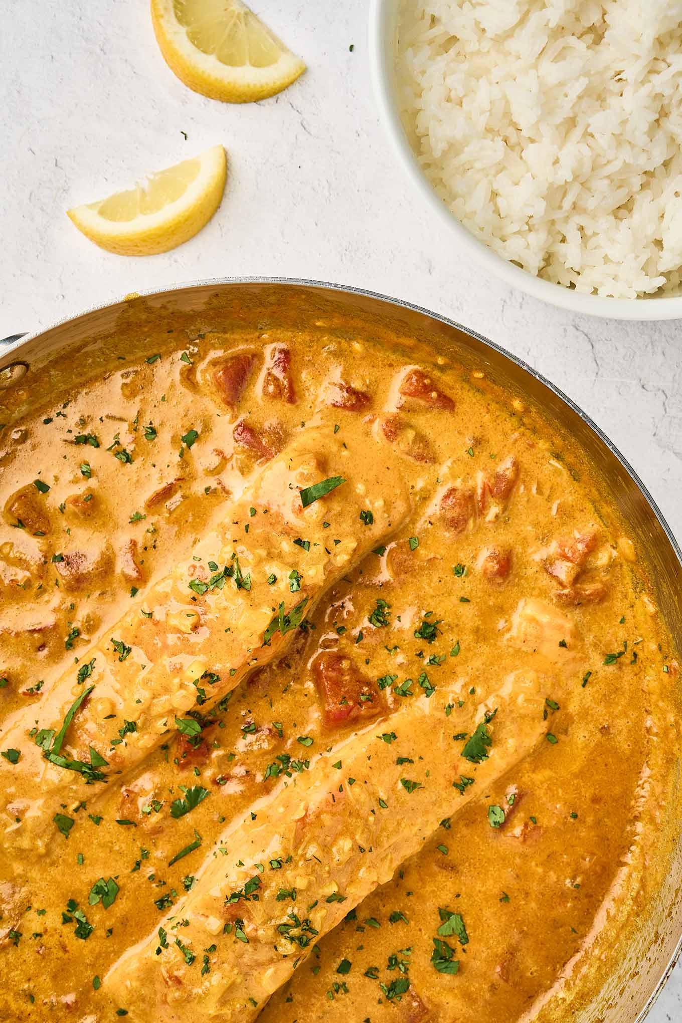Coconut curry salmon in a skillet with creamy coconut curry sauce, diced tomatoes, and fresh cilantro.