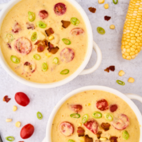 Two white crocks filled with fresh corn and potato chowder with bacon and tomatoes.