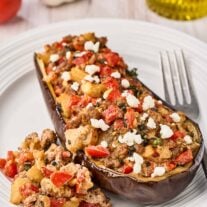 Mediterranean stuffed eggplant with lamb topped with goat cheese, served on a white plate.
