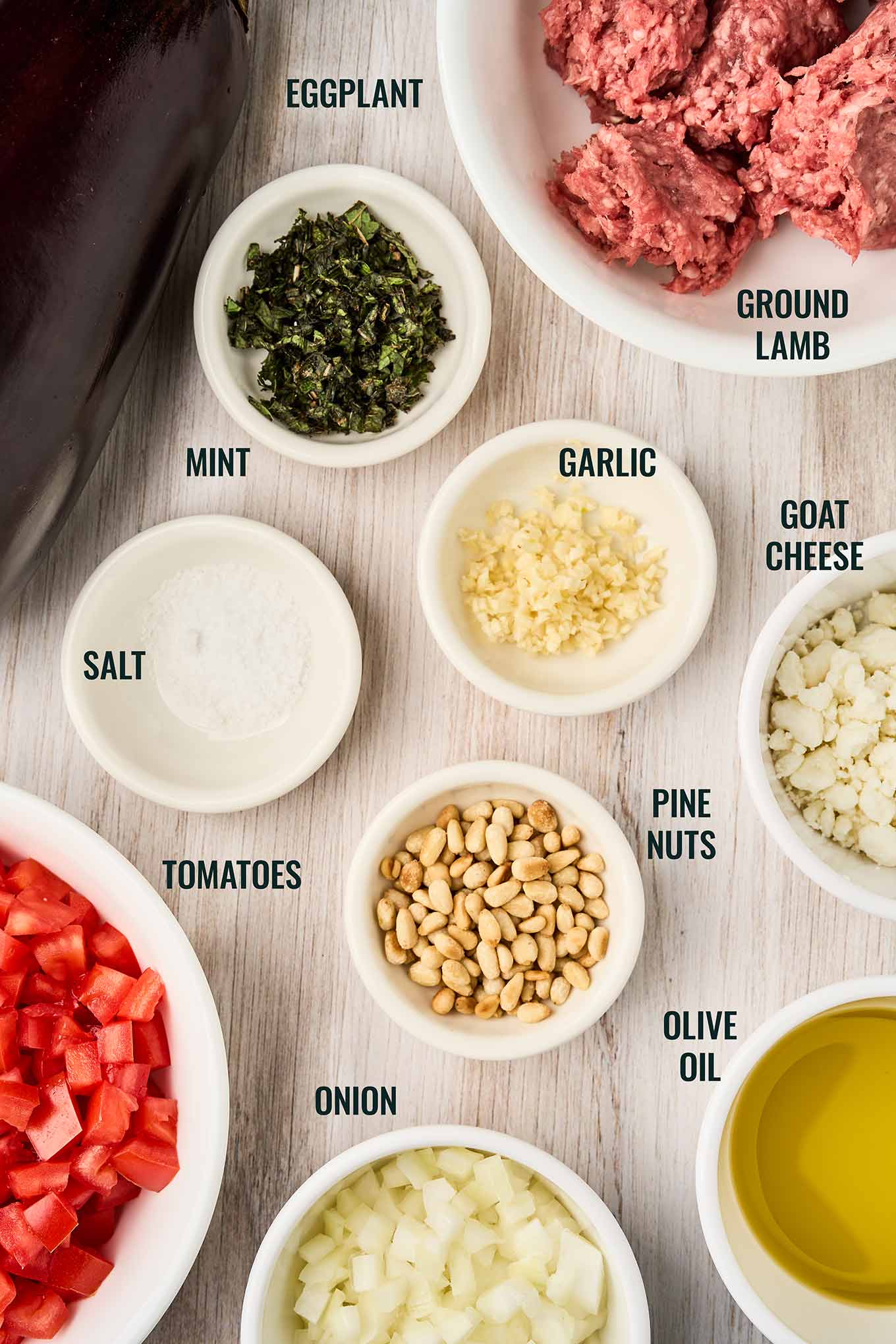 Ingredients for Mediterranean stuffed eggplant with lamb, including eggplant, ground lamb, tomatoes, goat cheese, mint, and pine nuts.