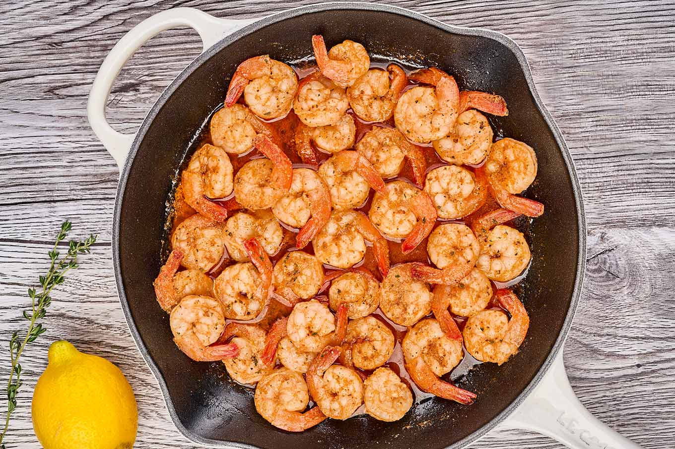 A cast iron skillet of shrimp saut&eacute;ed in butter with Old Bay seasoning, lemon, and fresh thyme.