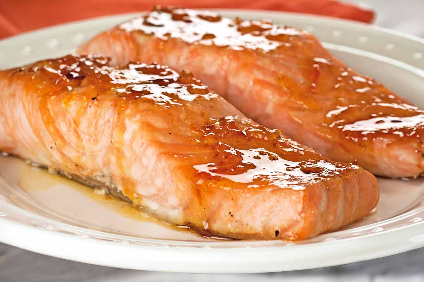 Close-up of two orange marmalade and bourbon glazed salmon on a white serving plate.