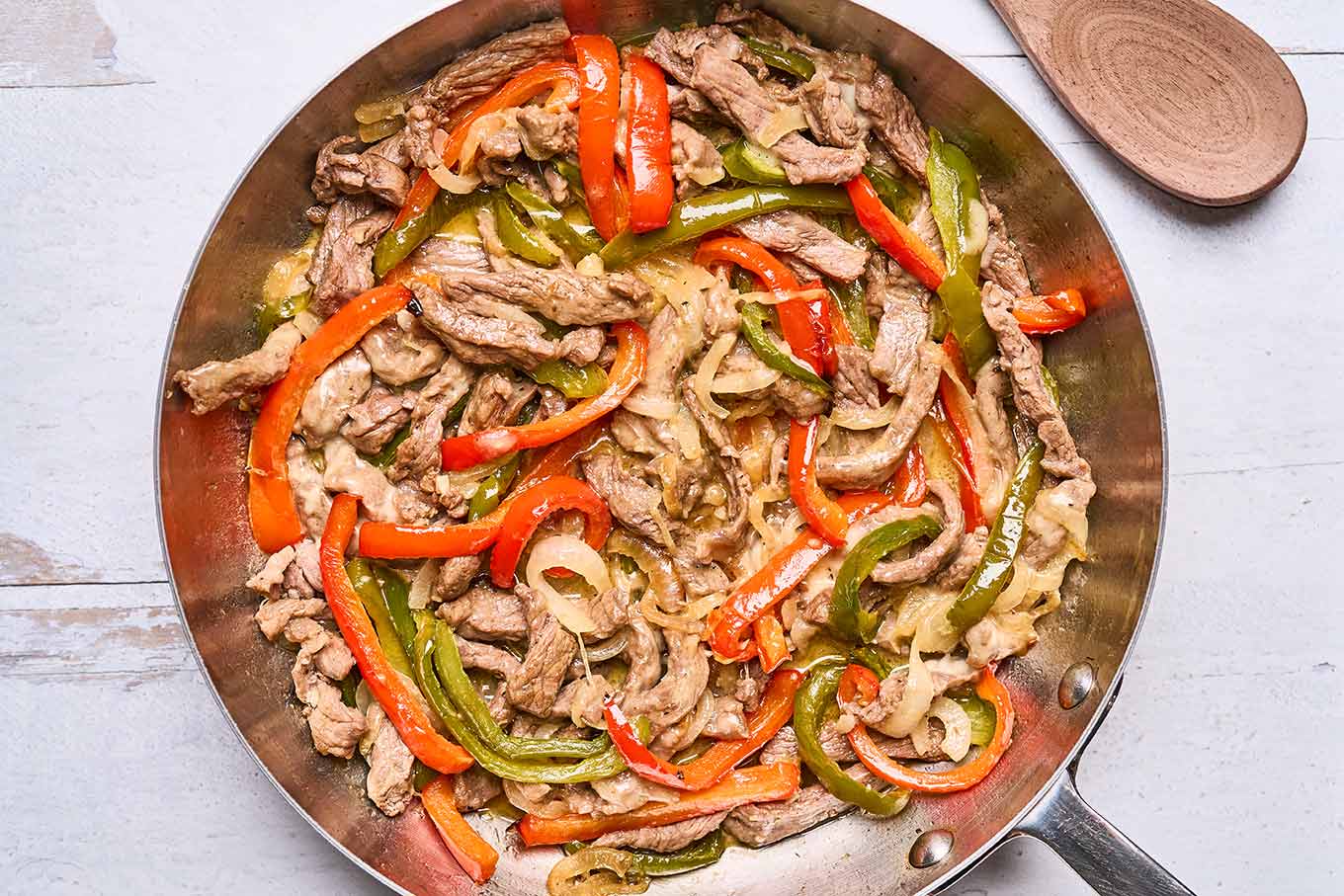 Cooked steak, roasted bell peppers, and sautéed onions combined in a skillet for Philly cheesesteak sandwiches.
