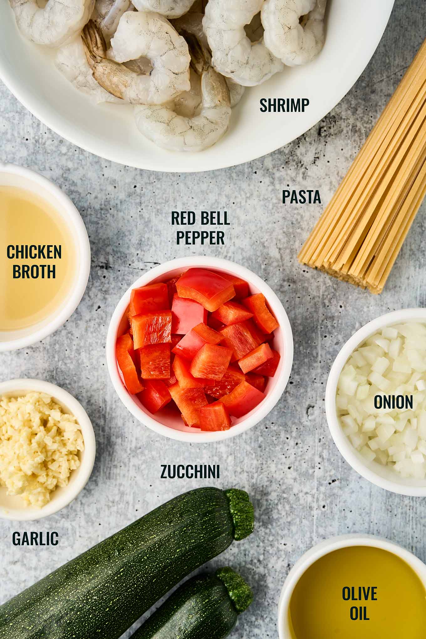 Ingredients for shrimp and zucchini pasta including shrimp, zucchini, red bell pepper, onion, garlic, linguine, chicken broth, and olive oil.
