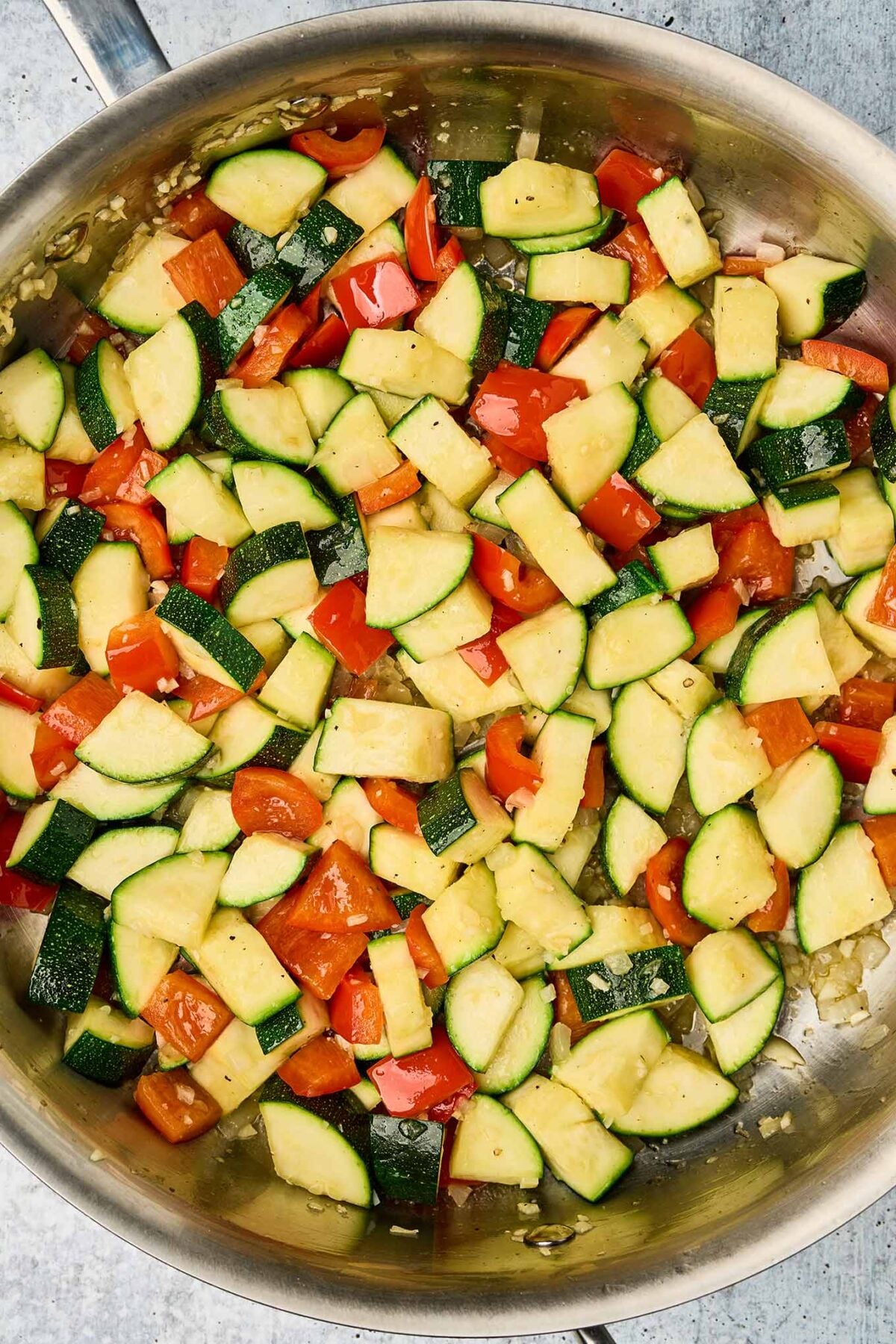 Zucchini, red bell pepper, onion, and garlic sautéing in a skillet for shrimp and zucchini pasta.