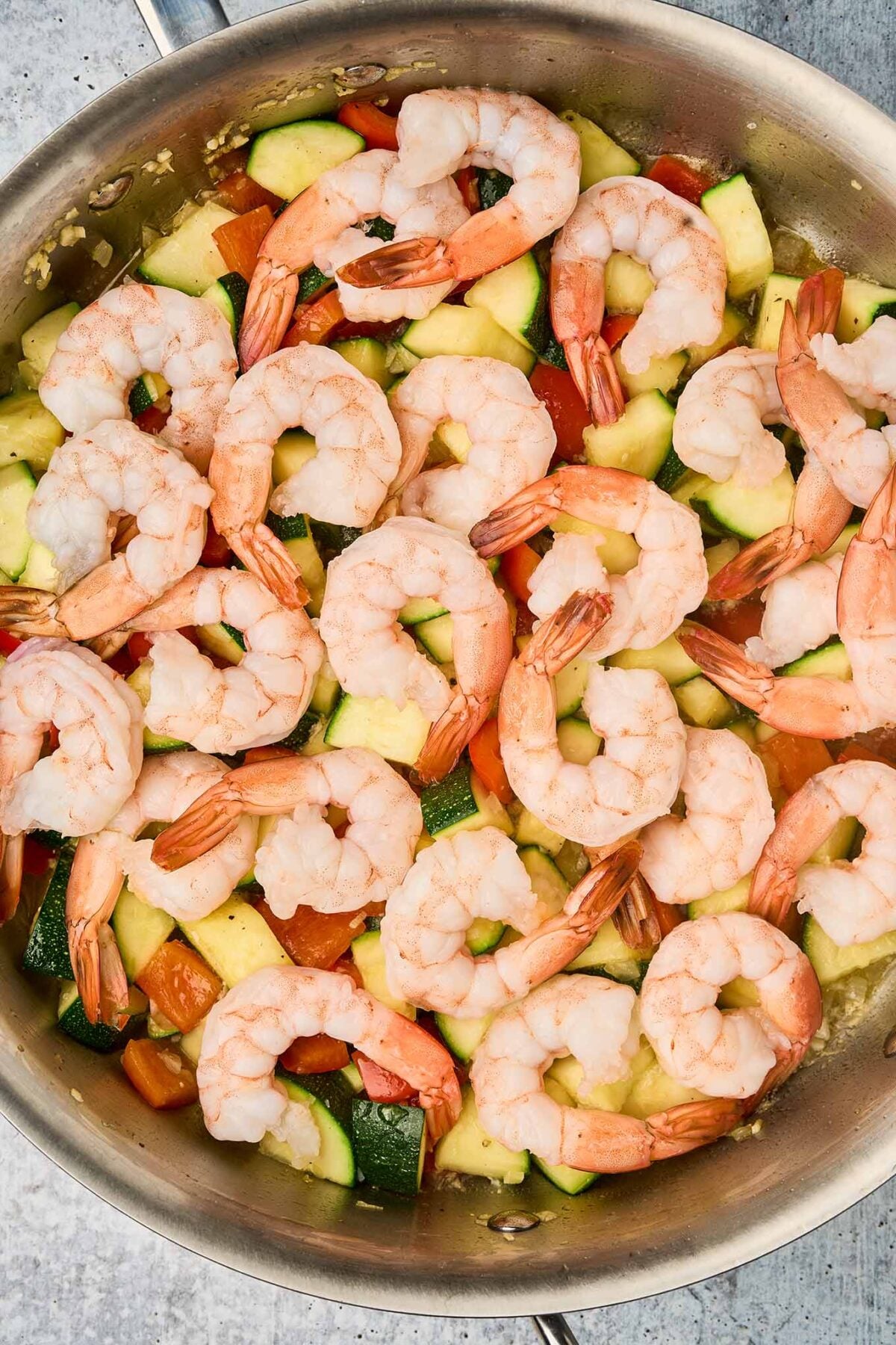 Shrimp arranged in a single layer over sautéed zucchini and bell pepper for even cooking.