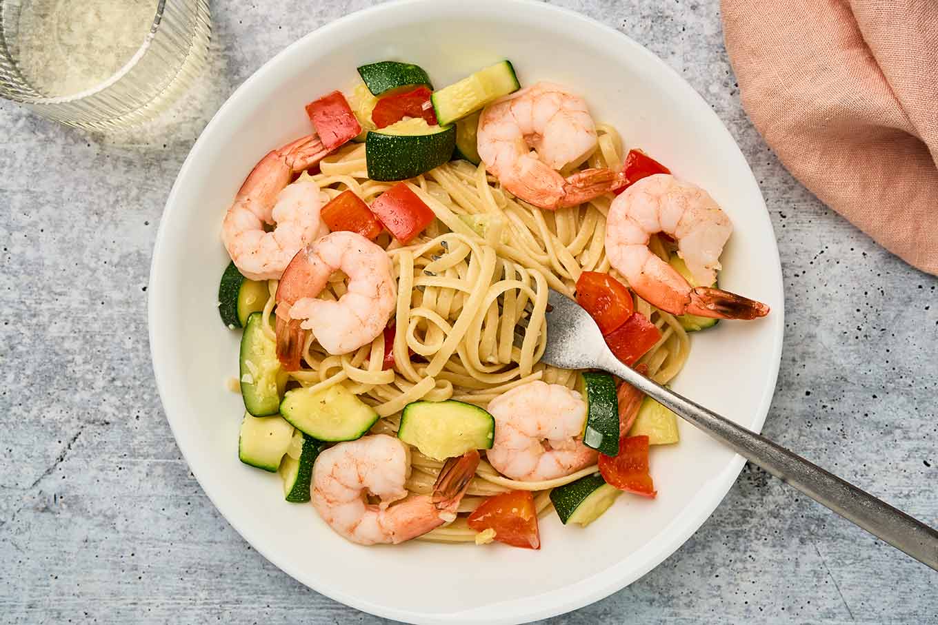 Plated shrimp and zucchini pasta with linguine, sautéed zucchini, and red bell pepper in a light garlic sauce.