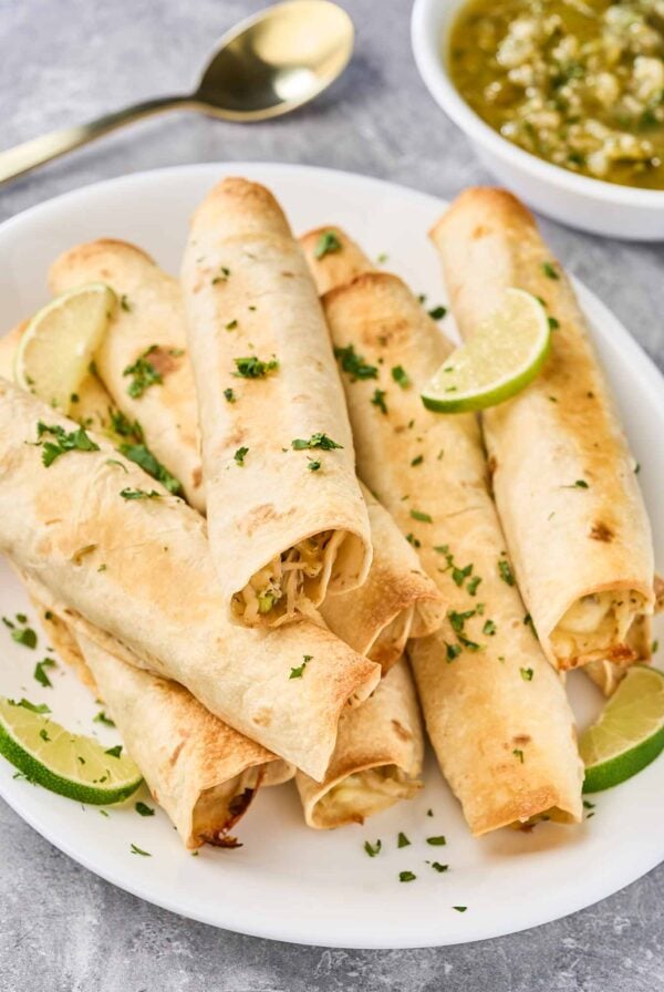 Baked chicken flautas garnished with cilantro and lime, served with fresh tomatillo sauce.