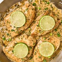 Creamy cilantro lime chicken in a skillet with fresh lime slices, scallions, and cilantro garnish.