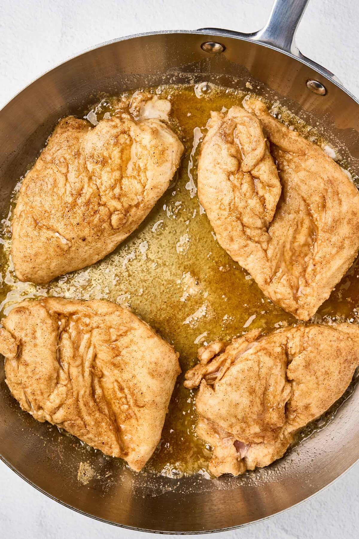 Seasoned chicken breasts browning in a skillet for creamy cilantro lime chicken.
