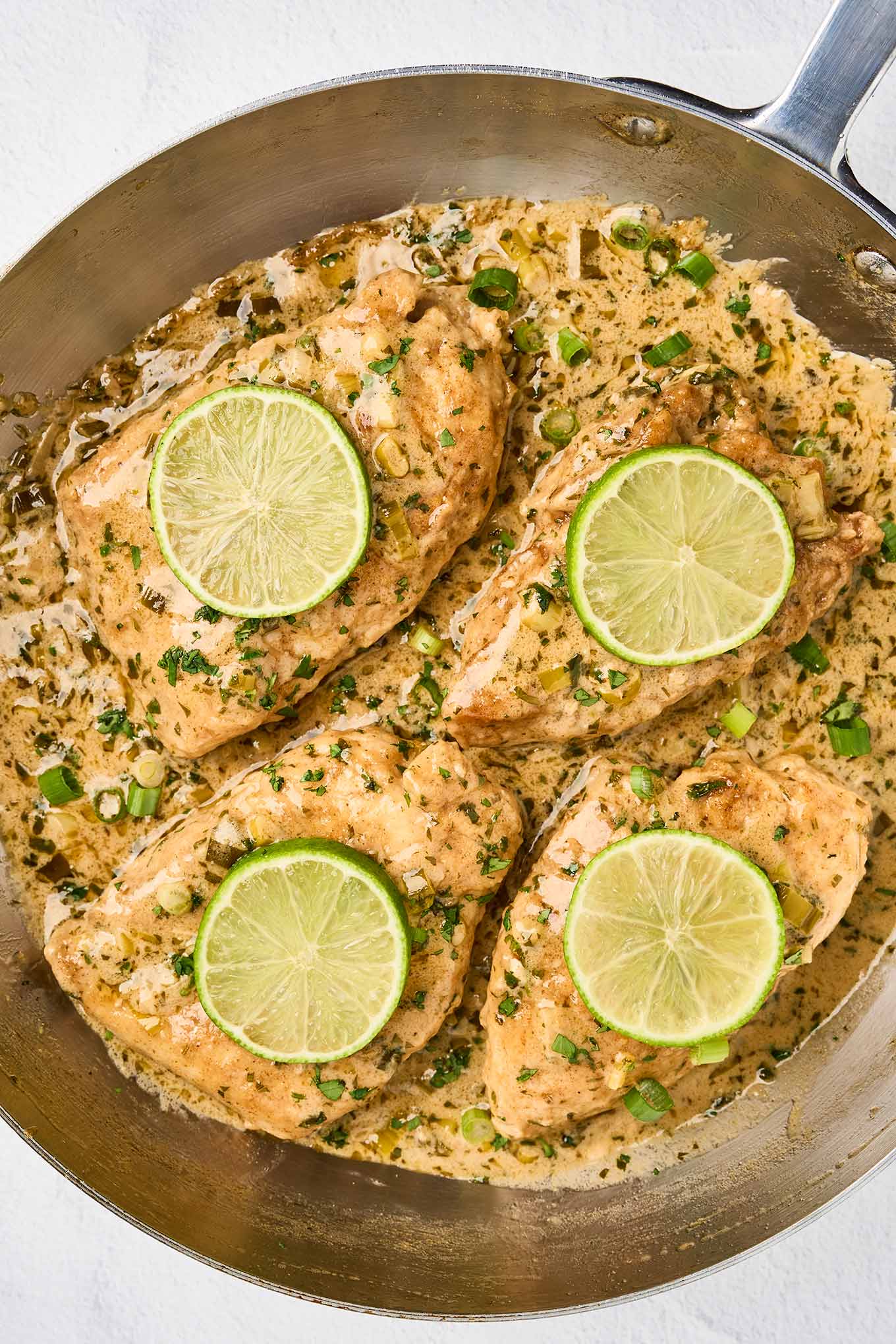 Creamy cilantro lime chicken in a skillet with fresh lime slices, scallions, and cilantro garnish.