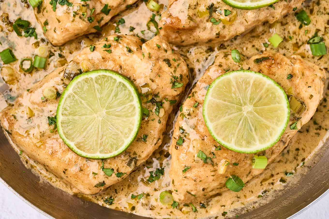 Close-up of creamy cilantro lime chicken in a light herb cream sauce with fresh lime slices.