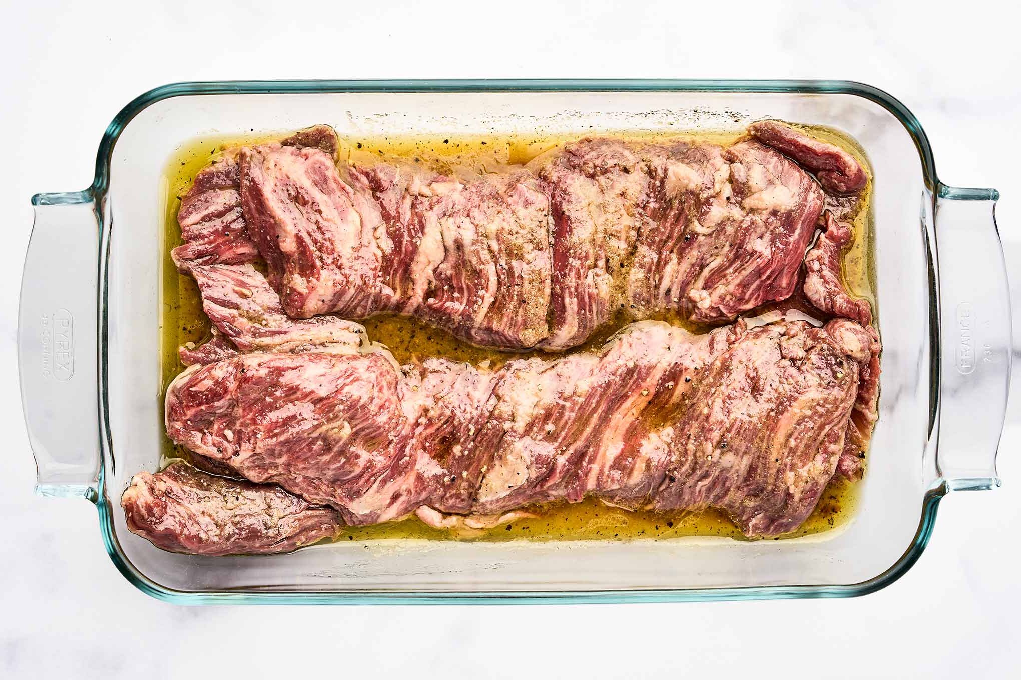 Skirt steak marinating with olive oil, citrus juice, Worcestershire sauce, and seasonings.