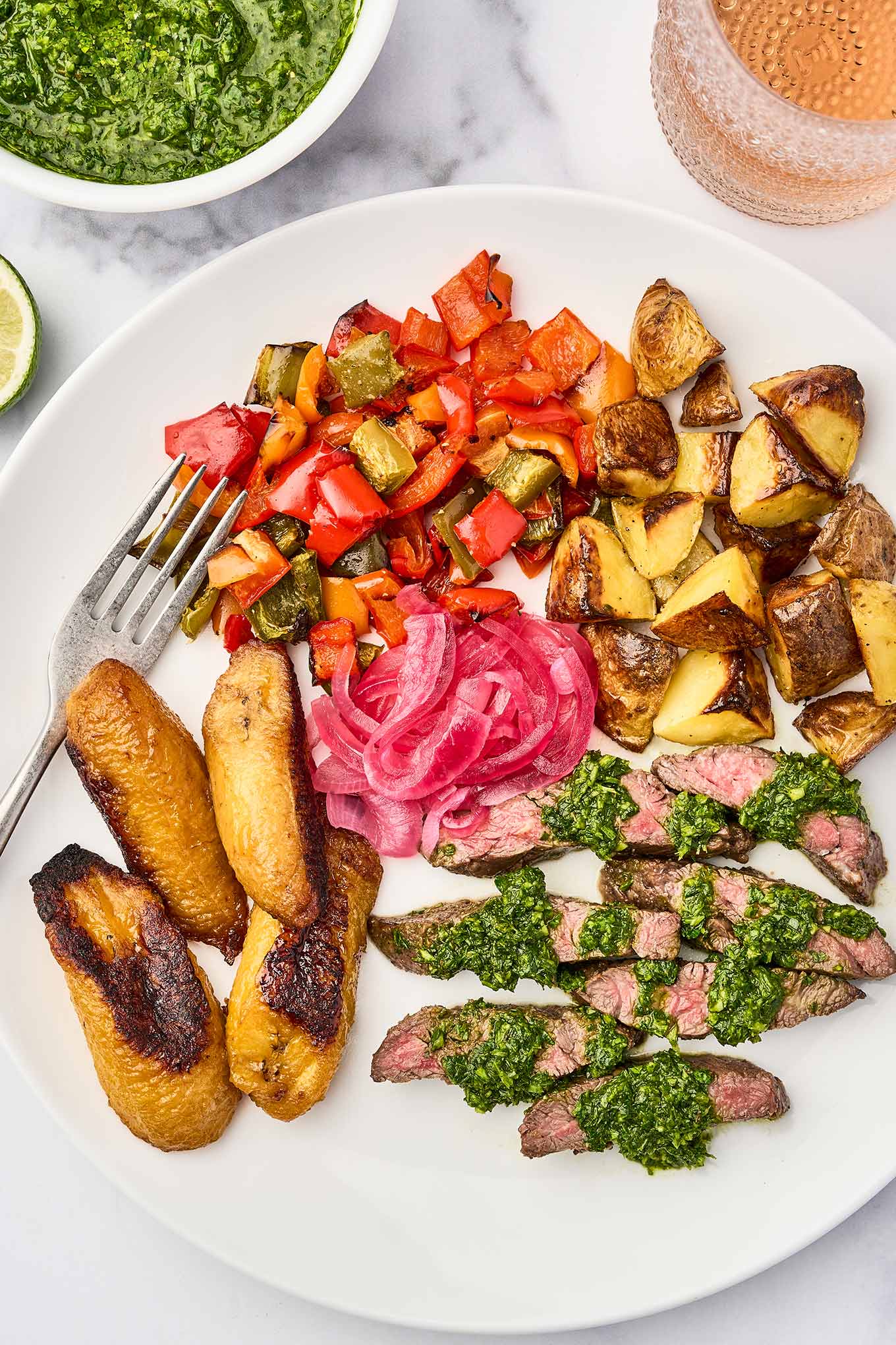 Grilled steak with chimichurri sauce served with roasted potatoes, roasted bell peppers, pickled red onions, and sweet plantains.