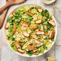 Mexican Caesar salad with chicken in a serving bowl with corn, queso fresco, toasted tortilla chips, and cilantro-lime dressing.