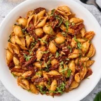 Sun-dried tomato pasta with balsamic and basil served in a white bowl, garnished with fresh basil.