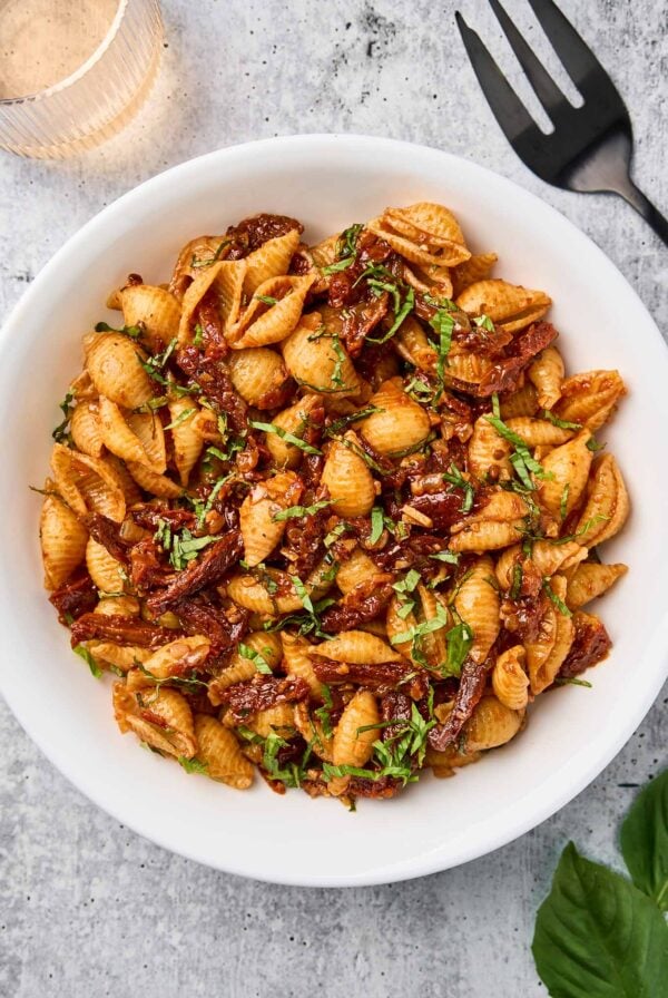 Sun-dried tomato pasta with balsamic and basil served in a white bowl, garnished with fresh basil.
