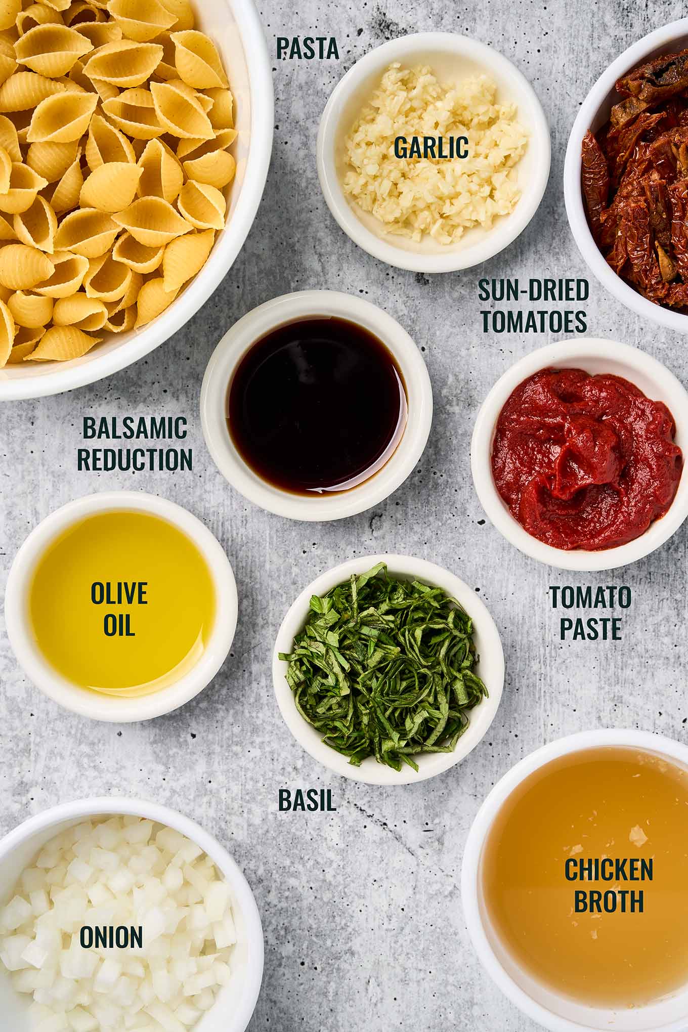 Labeled ingredients for sun-dried tomato pasta, including shell pasta, sun-dried tomatoes, basil, balsamic reduction, and garlic.