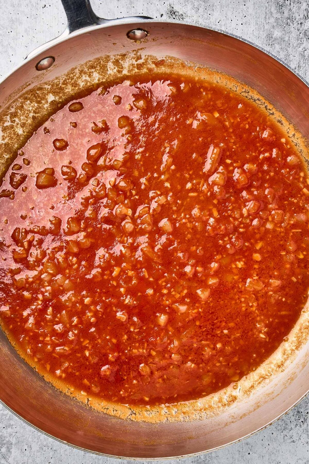 Chicken broth and tomato paste simmering with onion and garlic for sun-dried tomato pasta.