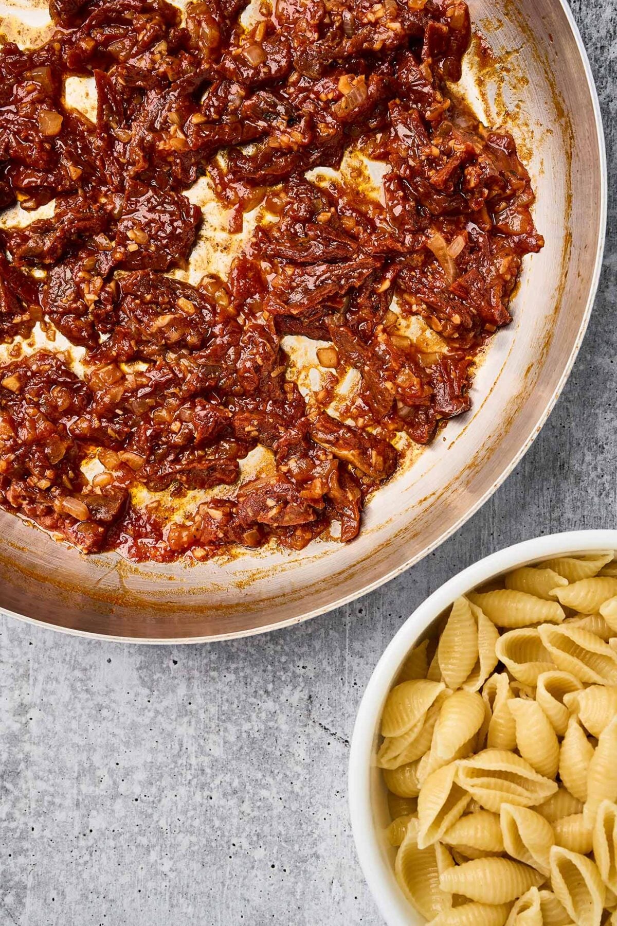 Sun-dried tomato sauce and cooked shell pasta ready to be combined.