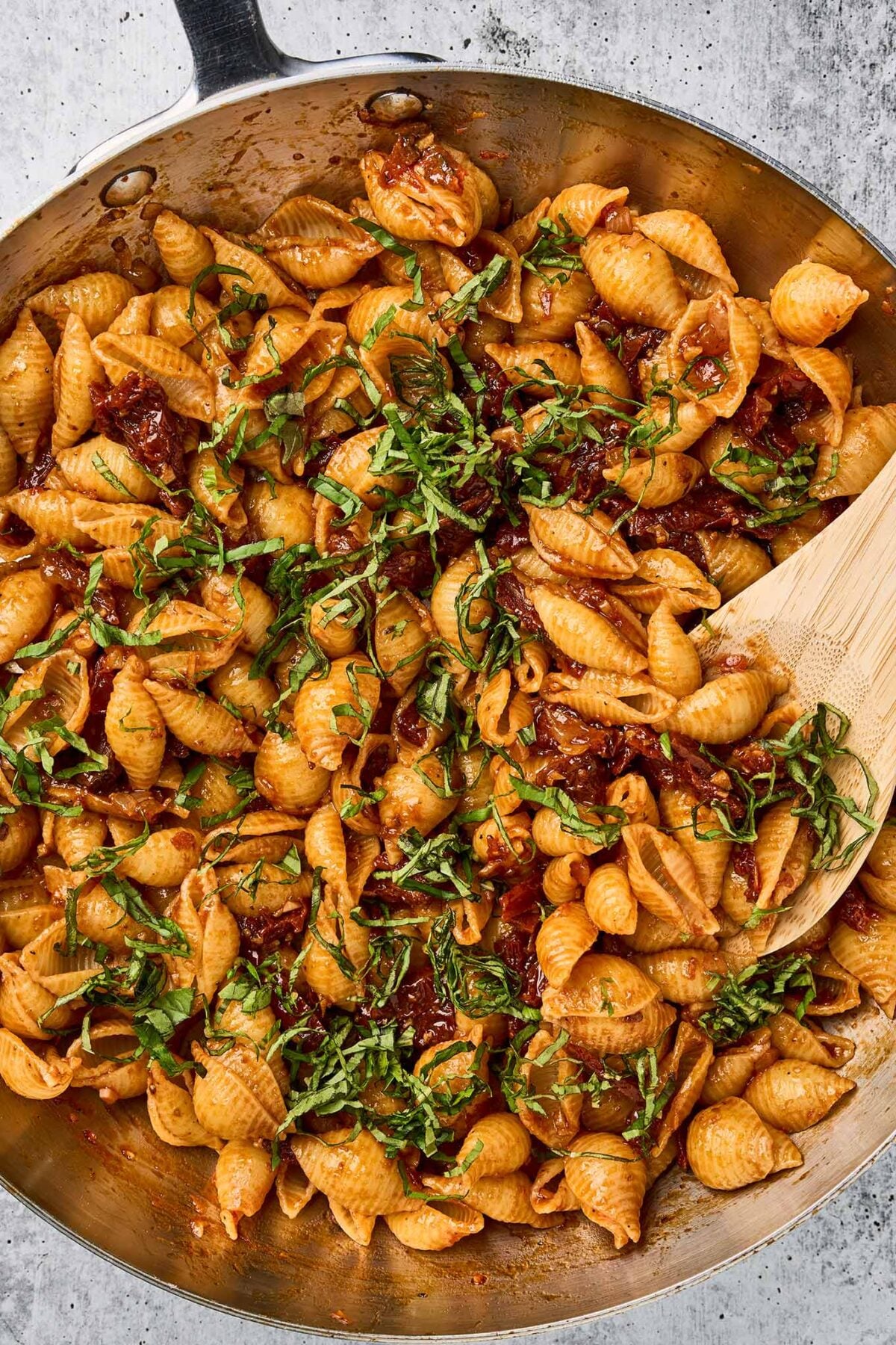 Fresh basil being folded into sun-dried tomato pasta before serving.