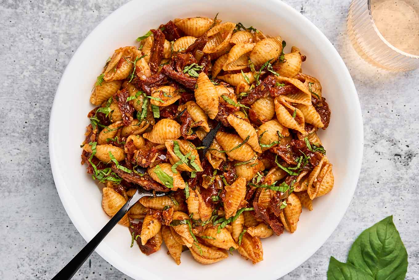 Sun-dried tomato pasta with balsamic and basil in a serving bowl with a serving spoon.