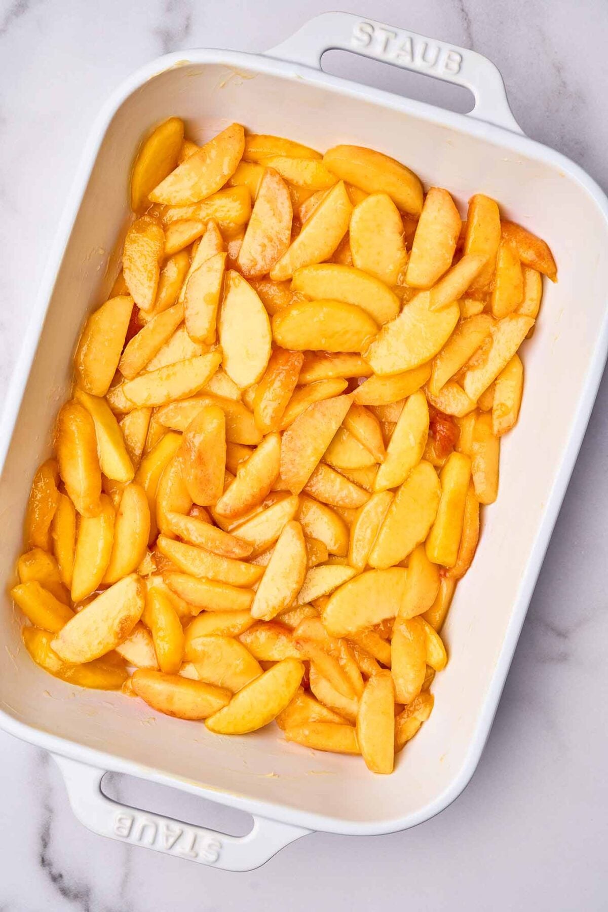 Sliced fresh peaches tossed with lemon juice and sugar in a baking dish for peach cobbler.