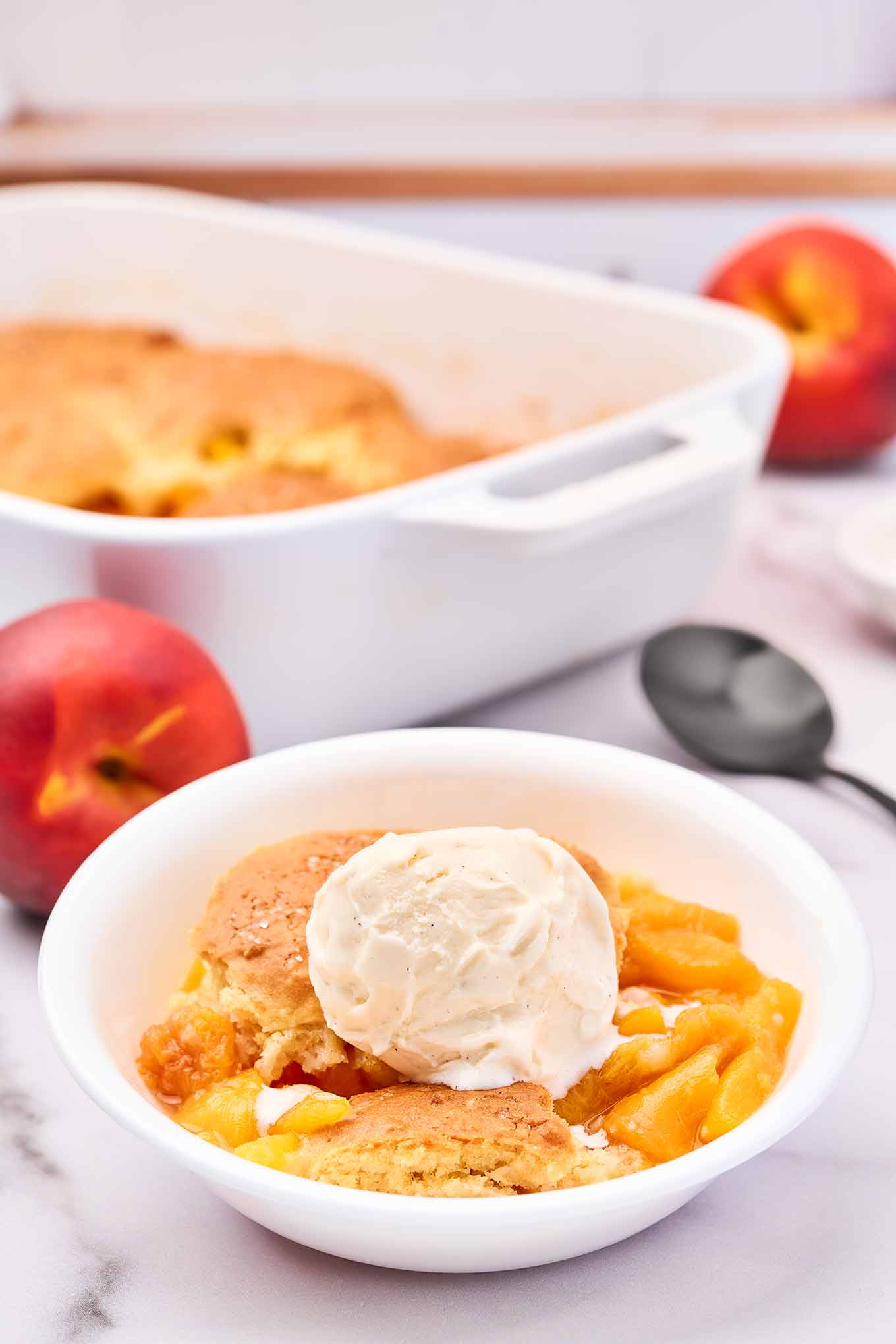 Fresh peach cobbler with biscuit topping and vanilla ice cream served in a white bowl.