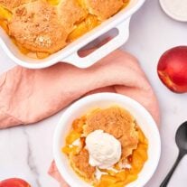 Fresh peach cobbler with biscuit topping and vanilla ice cream served in a white bowl, viewed from above.
