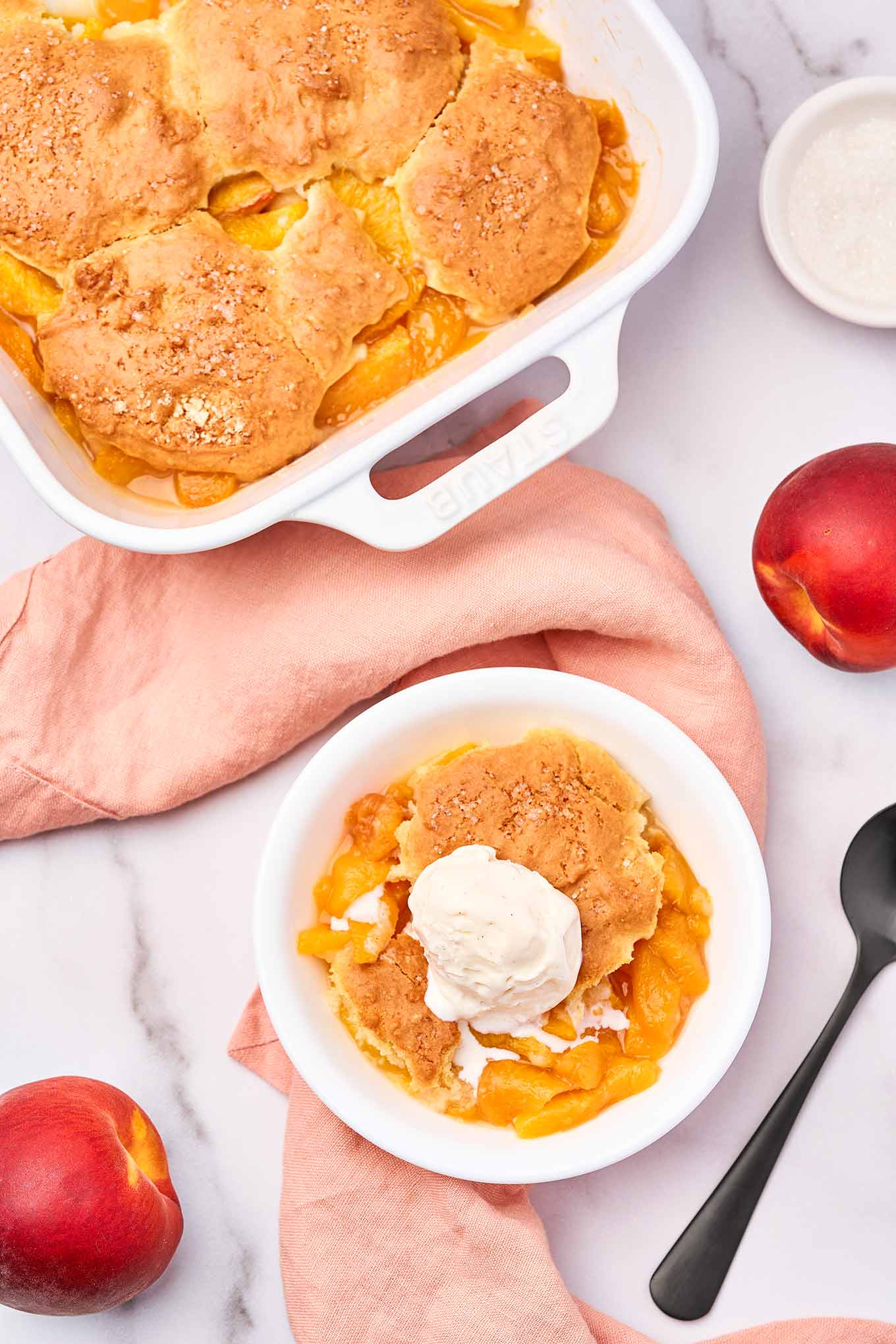 Fresh peach cobbler with biscuit topping and vanilla ice cream served in a white bowl, viewed from above.