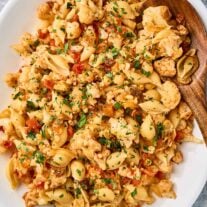 Sicilian pasta with cauliflower, shell pasta, tomatoes, raisins, pine nuts, and chopped parsley on a white platter.