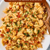 Sicilian pasta with cauliflower, shell pasta, tomatoes, raisins, pine nuts, and parsley garnish on a serving platter.