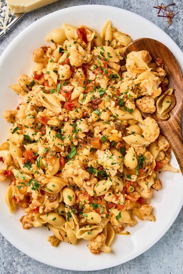 Sicilian pasta with cauliflower, shell pasta, tomatoes, raisins, pine nuts, and chopped parsley on a white platter.