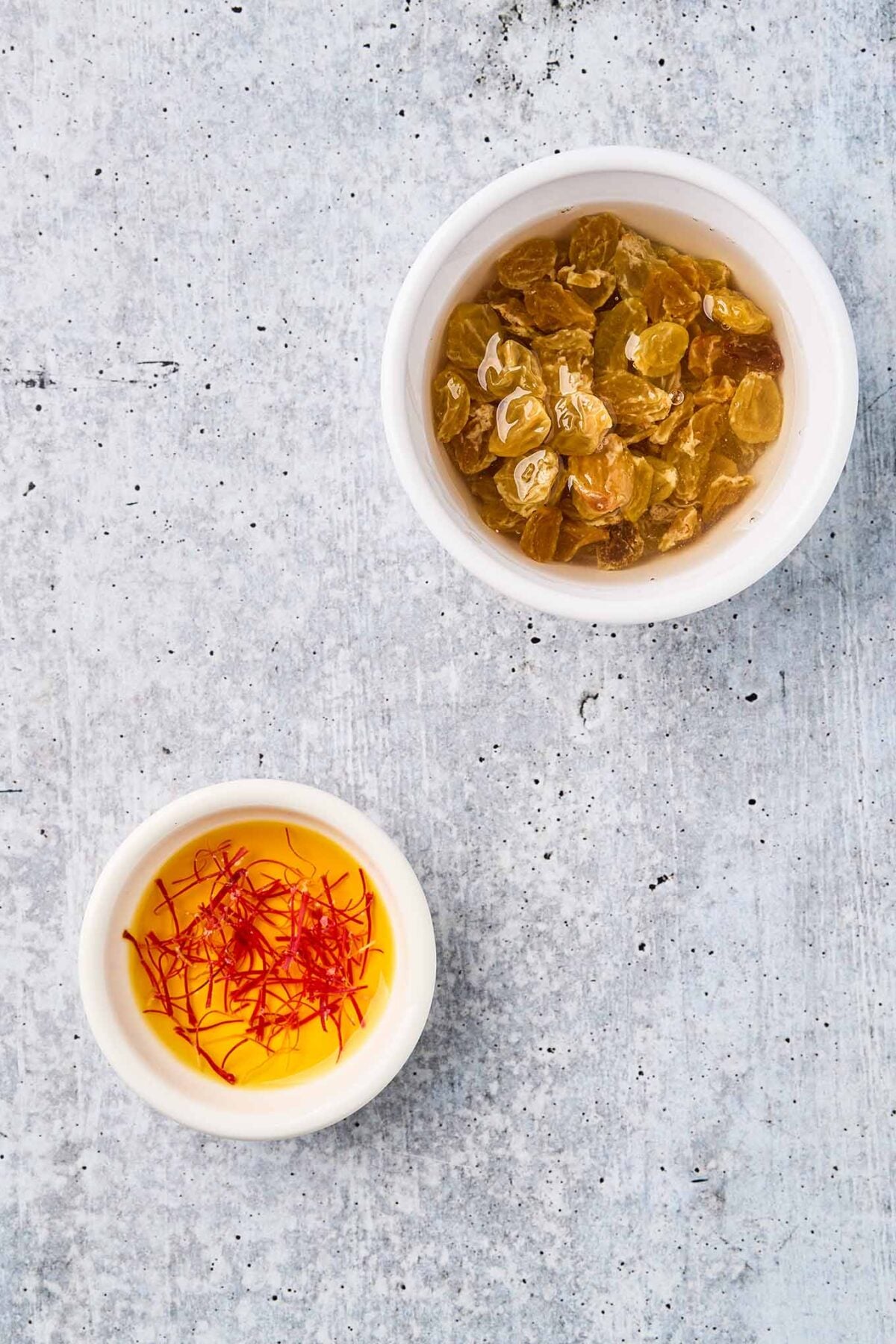 Saffron threads steeping and golden raisins plumping in hot water.