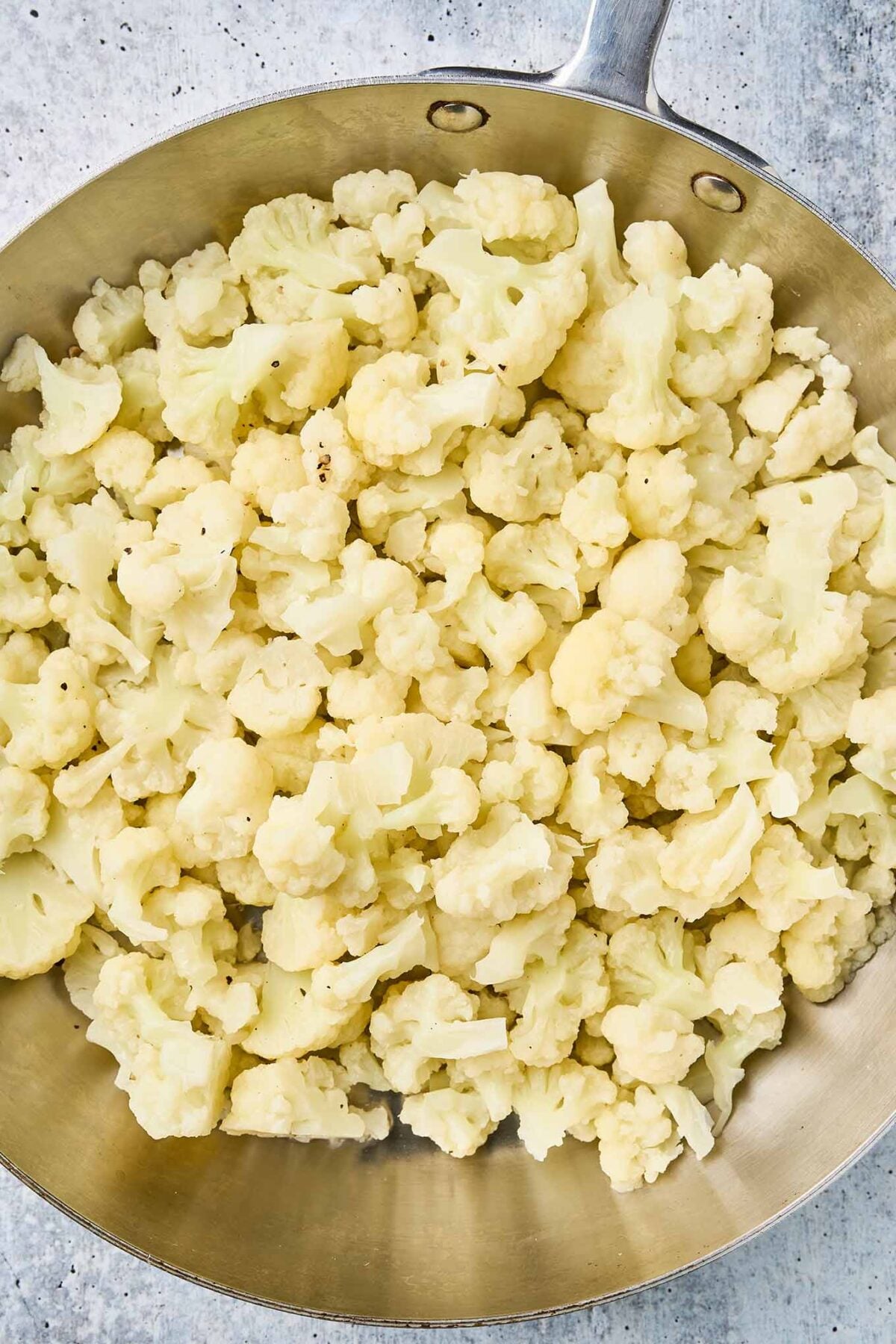 Cauliflower florets simmering in a skillet until tender.