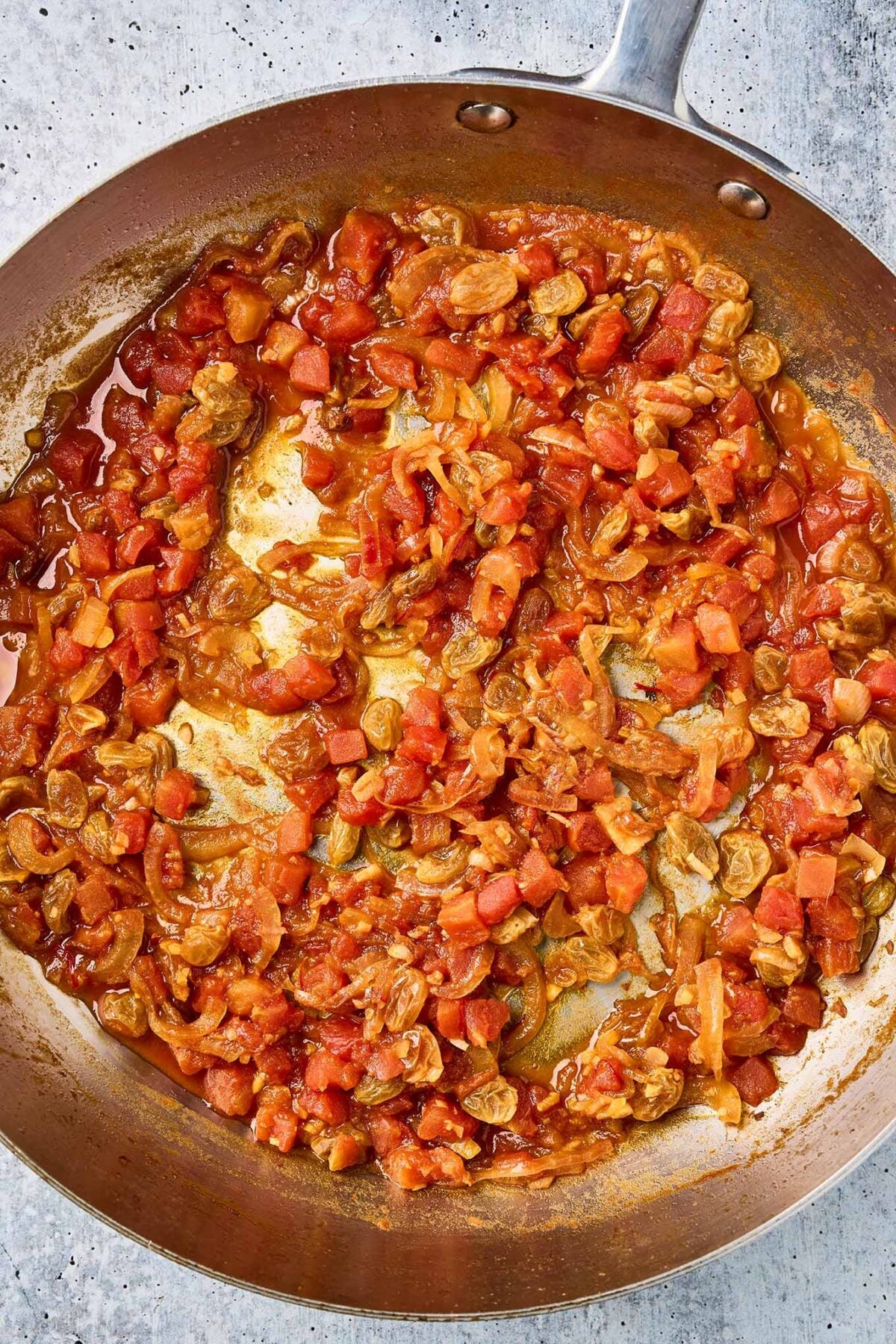 Onion, garlic, tomatoes, saffron, and plumped raisins simmering in a skillet.